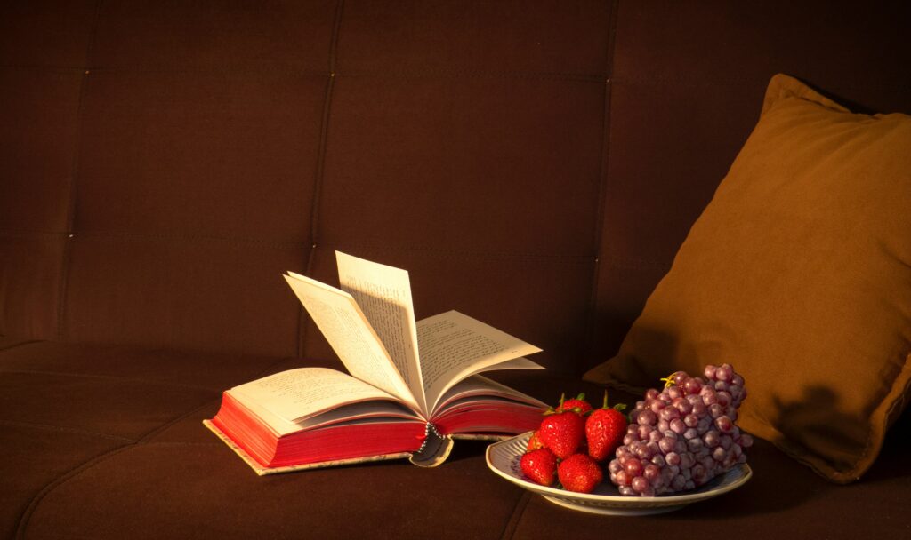 Strawberries sitting on a couch along a book and some other berries